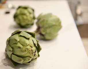 Obraz premium Three green artichokes sitting on marble