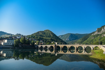 Fototapeta na wymiar The Ottoman Mehmed Pasa Sokolovic Bridge in Visegrad, Bosnian mountains, with fantastic sky scape and river reflection. Bosnia and Herzegovina.