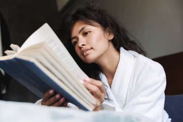Photo of adorable woman wearing housecoat reading book in bed at home