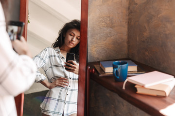 Fototapeta na wymiar Photo of woman taking selfie photo and looking at mirror in apartment
