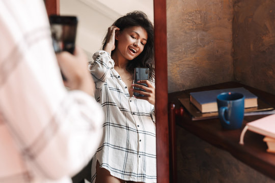 Photo of woman taking selfie photo and looking at mirror in apartment