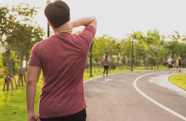 A male athlete suffering from neck pain and injury at the park. Sport and healthcare concept.