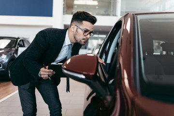 Car seller working in showroom and quality control checking of car details for the last time before...