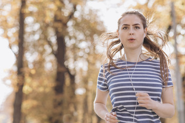 Female jogger running on road and street in park with trees. Woman in jogging trail in the morning. Runner doing outdoor cardio exercise in sunny day. Person training for marathon.