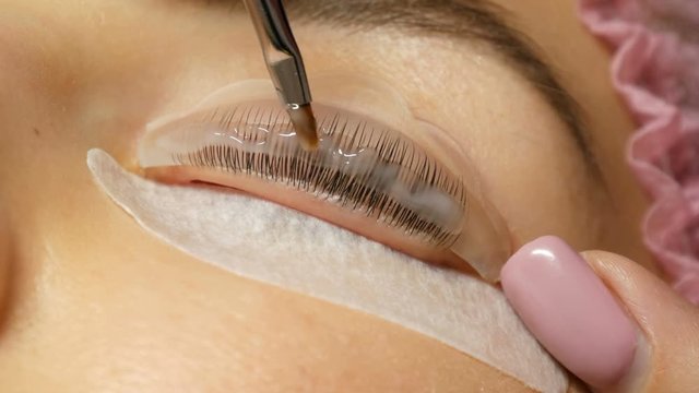 Beautician applies a special wellness mixture on client eyelashes close up view. Professional procedure laminating and Botox eyelashes modern healing. Silicone curlers or rollers for curling