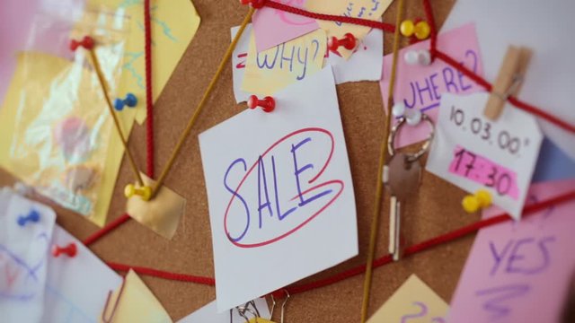 Discount search concept. Close-up view of a detective board with evidence. In the center Girl's hand pins a white sheet of paper with the inscription Sale