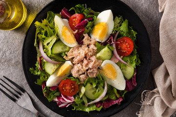 Salad with tuna, egg and vegetables on black plate and gray background. Top view	