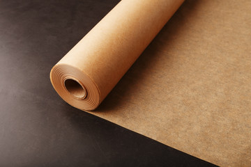 A roll of unfolded brown parchment paper, for baking food in on a dark background, top view.