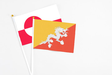 Bhutan and Greenland stick flags on white background. High quality fabric, miniature national flag. Peaceful global concept.White floor for copy space.