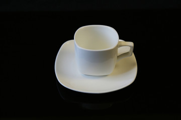 Isolated white coffee cup with saucer on a black background with copy space for text. The cup is empty. Coffee background.