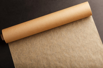 A roll of unfolded brown parchment paper, for baking food in on a dark background, top view.
