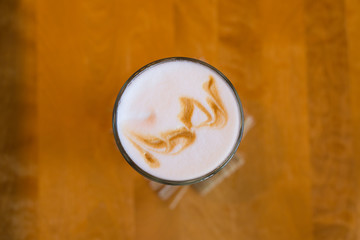 A glass of cappuccino stands on a wooden table, top view.