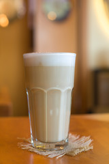Glass of cappuccino stands on a wooden table.
