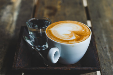 close up modern hot black coffee the cappuccino on wood background with coffee bubble foam pattern and texture in white cup looking and feel so delicious on glasses table in coffee shop.