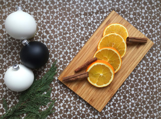 A decorative composition with orange slices and cinnamon on the wooden board, cypress branch and Christmas decorations