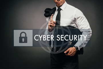 cropped view of african american businessman holding blazer and leather briefcase on dark background with cyber security illustration