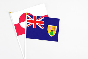 Fototapeta premium Turks And Caicos Islands and Greenland stick flags on white background. High quality fabric, miniature national flag. Peaceful global concept.White floor for copy space.