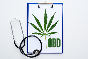 top view of medical cannabis leaf on clipboard with cbd lettering near stethoscope on white background