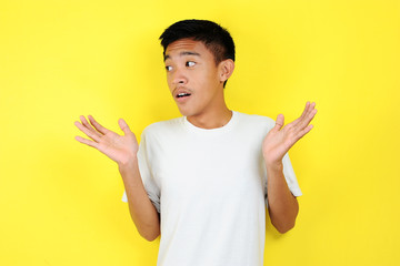 Maybe yes or no. Doubtful Young Asian man shrugs shoulders in bewilderment, tries to make decision,...
