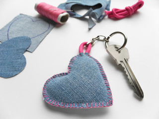 Handmade denim heart keychain with key. Cuted cloth, spool of thread with needle, pink cord on background. Handmade gift. Valentine's day concept. 