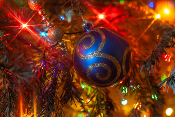 Decorations on a fir-tree: shiny blue ball with ornament is illuminated by red light on the blurred christmas background