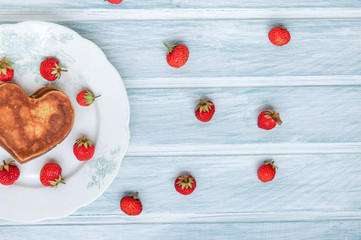 Fototapeta na wymiar Pancakes and strawberry on a light blue white background. Heart shaped pancakes for boy friend