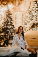 Pretty woman sits against background of Christmas decorations and retro car.