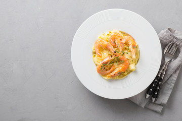 Pasta spaghetti reginelle with seafood, shrimps white plate on gray stone table, view from above. Traditional dish in Italian. Space for text.