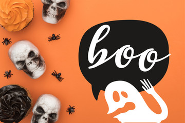 top view of cupcakes, decorative skulls and spiders on orange background with boo and ghost illustration