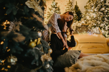 Lesbian couple hugs against background of Christmas decorations and retro car.