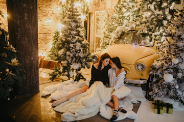 Lesbian couple hugs against background of Christmas decorations and retro car.