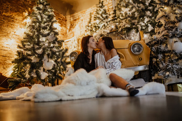 Lesbian couple kisses against background of Christmas decorations and retro car.