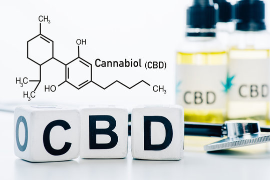 selective focus of cubes with cbd lettering near oil and stethoscope isolated on white with cbd molecule illustration