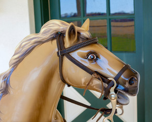 Close up of coin-operated horsehead amusement ride with stable in background.