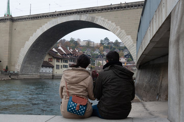 Pareja de espaldas sobre r&iacute;o mirando puente de piedra
