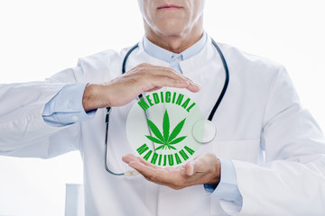 cropped view of doctor in white coat holding hands around medicinal marijuana illustration isolated on white