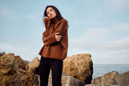 Attractive casual Asian girl in knitted sweater sensually posing by the sea