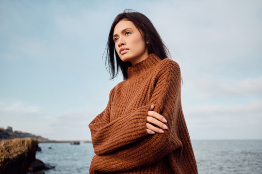 Gorgeous Asian brunette girl in knitted sweater sensually looking away on seaside