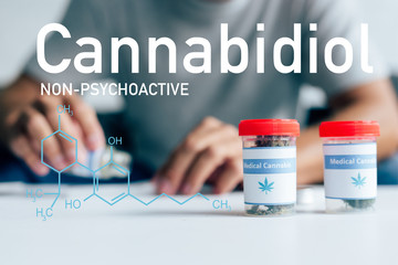 selective focus of bottles with medical cannabis on table with man on background with non-psychoactive cbd illustration
