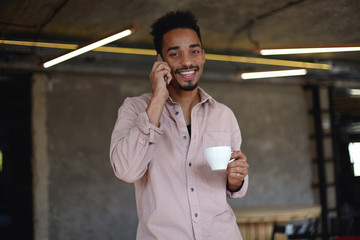 Portrait of lovely young bearded man with dark skin looking at camera cheerfully with wide charming...