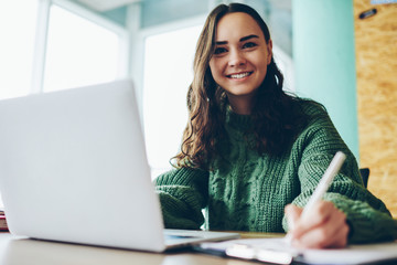 Portrait of smiling female student doing homework via netbook satisfied with online course,...