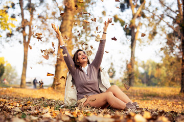 Young woman sitting on the ground in park with falling leafs
