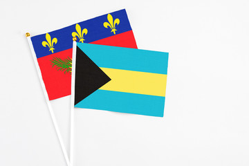 Bahamas and Guadeloupe stick flags on white background. High quality fabric, miniature national flag. Peaceful global concept.White floor for copy space.