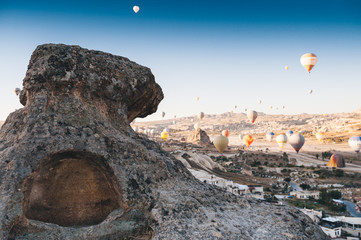 Hot air balloon flying over rock landscape in Cappadocia. Ancient cave in front of