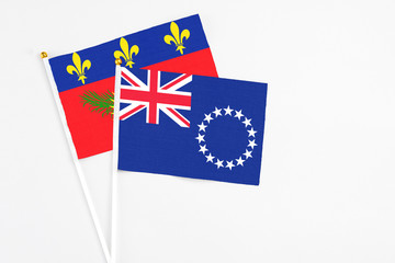 Fototapeta premium Cook Islands and Guadeloupe stick flags on white background. High quality fabric, miniature national flag. Peaceful global concept.White floor for copy space.