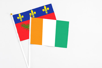 Cote D'Ivoire and Guadeloupe stick flags on white background. High quality fabric, miniature national flag. Peaceful global concept.White floor for copy space.