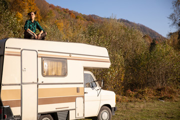 Caucasian girl sitting on the roof of a camper in a beautiful autumn landscape