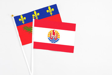 French Polynesia and Guadeloupe stick flags on white background. High quality fabric, miniature national flag. Peaceful global concept.White floor for copy space.