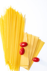 Dry spaghetti on a white background. Cherry tomatoes on a yellow pasta background. Italian pasta. Copy space