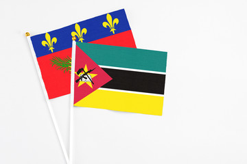 Mozambique and Guadeloupe stick flags on white background. High quality fabric, miniature national flag. Peaceful global concept.White floor for copy space.